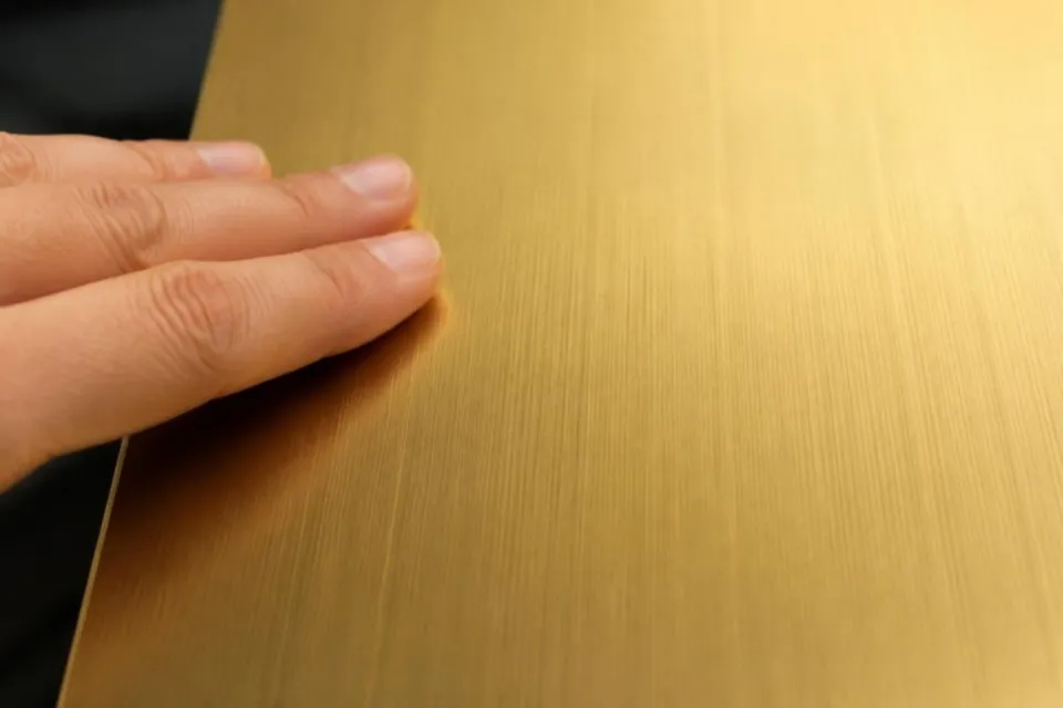 Fingertips on a gold hairline stainless steel sheet with anti-fingerprint coating